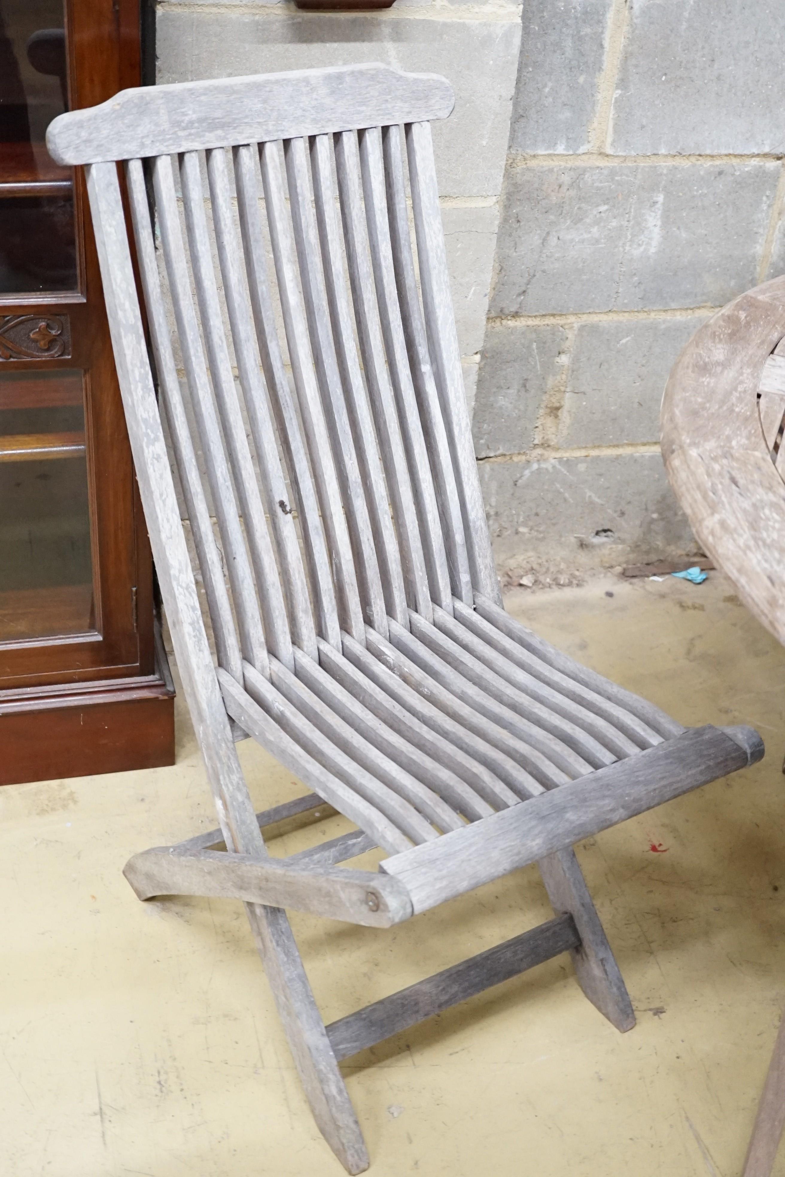 A weathered teak circular folding garden table, diameter 116cm and two pairs of folding chairs